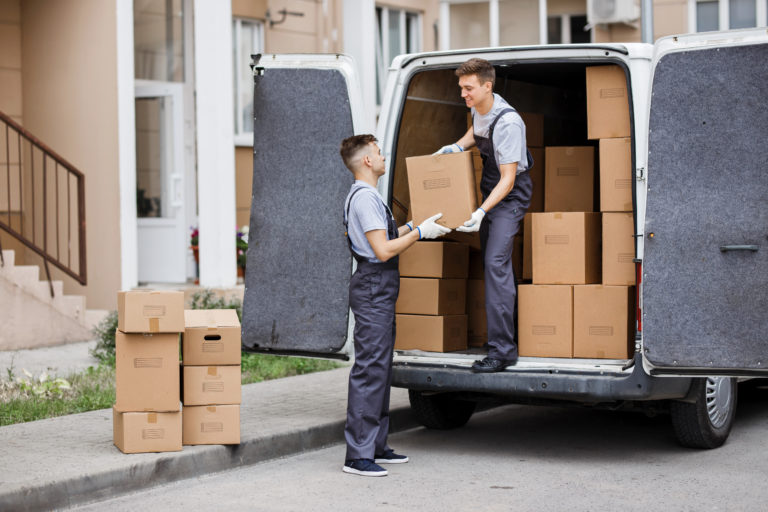 Two young handsome movers wearing uniforms are unloading the van full of boxes. House move, mover service